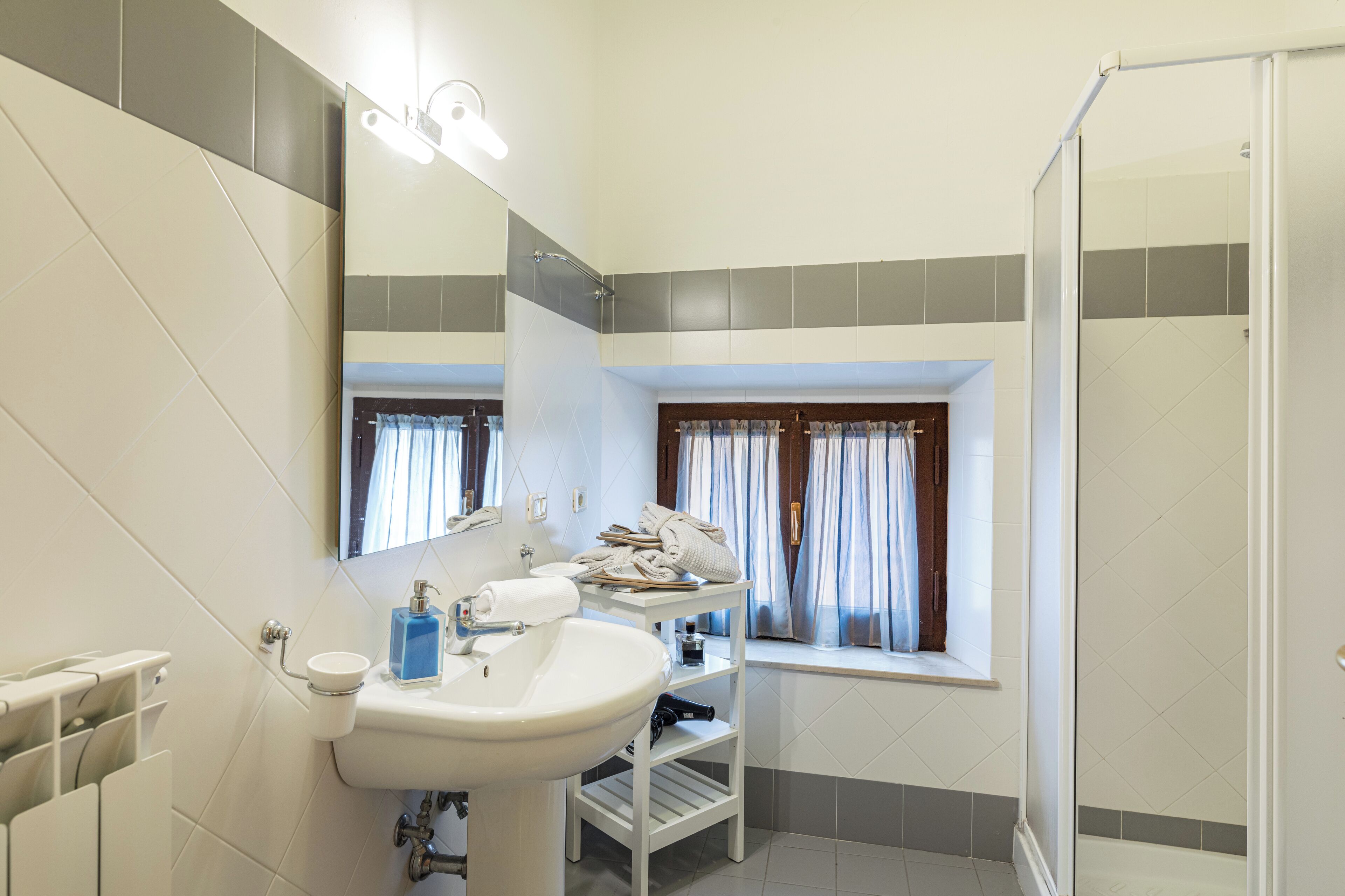 Ein Badezimmer mit Waschbecken, Spiegel, Dusche und einem Fenster mit Vorhängen.