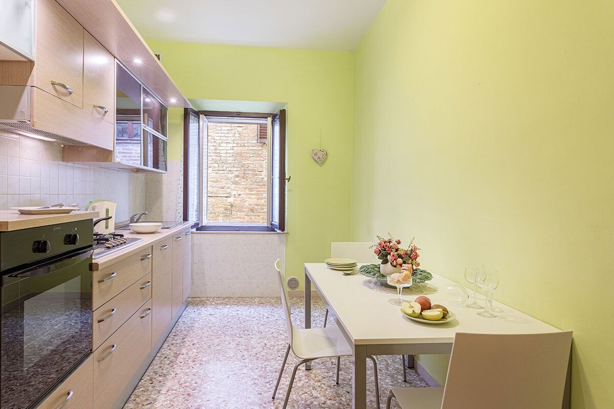 A compact kitchen with a dining area, a window, and a heart-shaped decoration on the wall.
