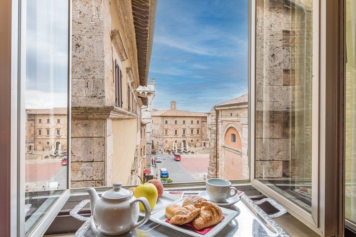 Un balcón con mesa dispuesta para el desayuno, vistas a edificios históricos y un cielo despejado.