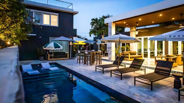 Un área de piscina moderna al aire libre con sillones y sombrillas, rodeada de arquitectura contemporánea.