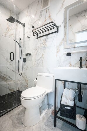 Une salle de bain moderne avec une douche en marbre, des toilettes et un lavabo équipé d’un porte-serviettes.