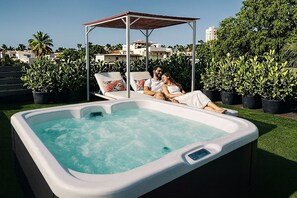 Una vasca idromassaggio con due poltrone relax e un gazebo immersi in un giardino.