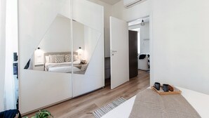 A modern bedroom with a mirrored wardrobe, a bedside table with a lamp, and a tray with mugs and pastries. - Nest & Rest (Como)