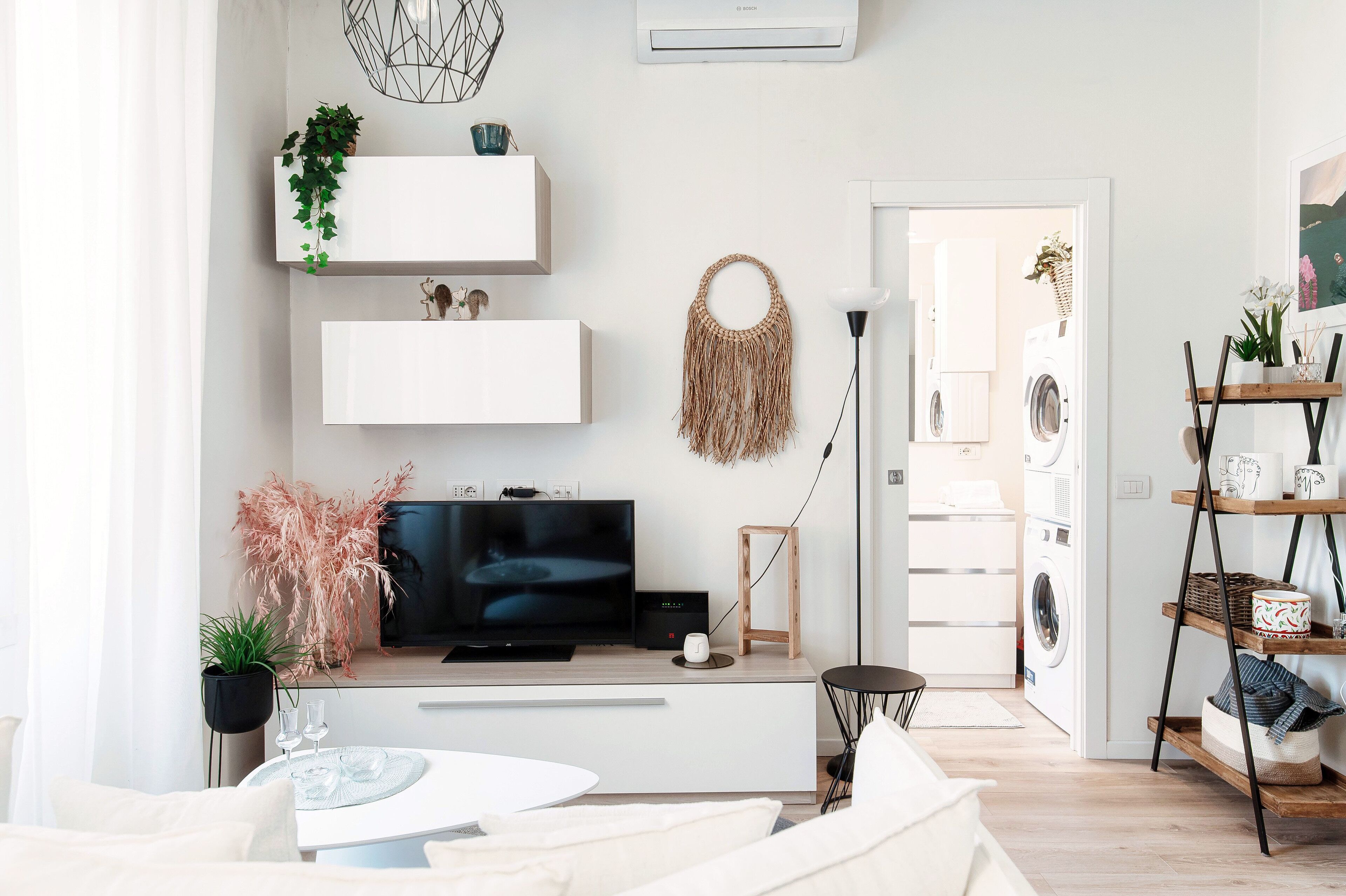 Una sala de estar moderna con un televisor de pantalla plana, sofás blancos, una mesa de centro y una zona de comedor con mesa y sillas.