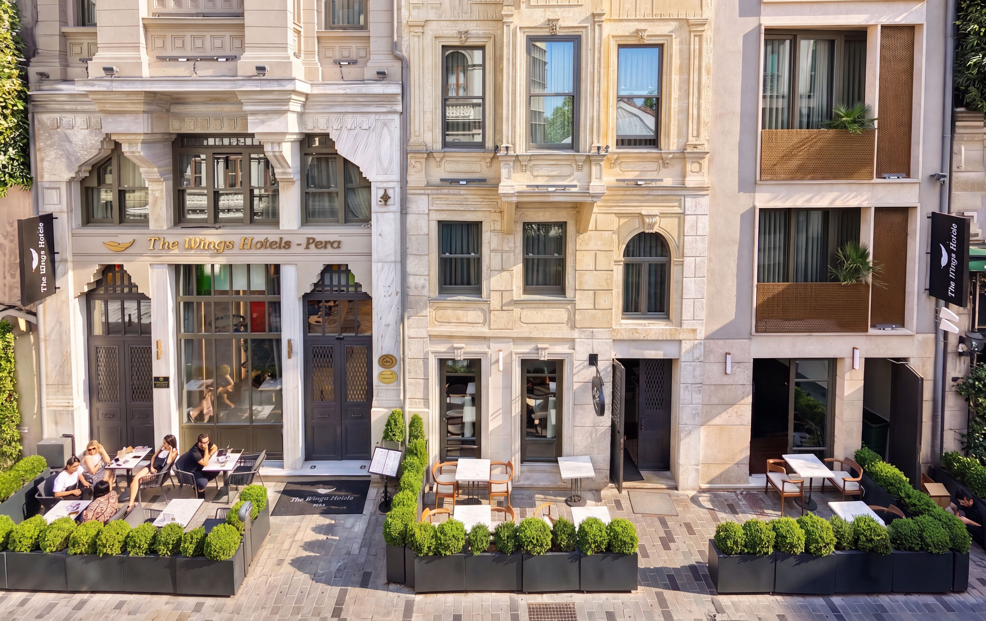 A hotel with a classic facade, outdoor seating, and a sign for 'The Wings Hotels - Pera'.