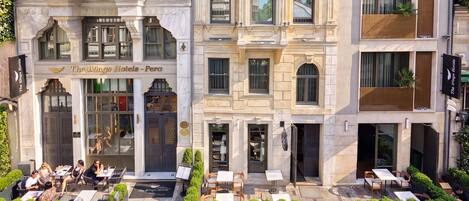 A hotel with a classic facade, outdoor seating, and a sign for 'The Wings Hotels - Pera'.