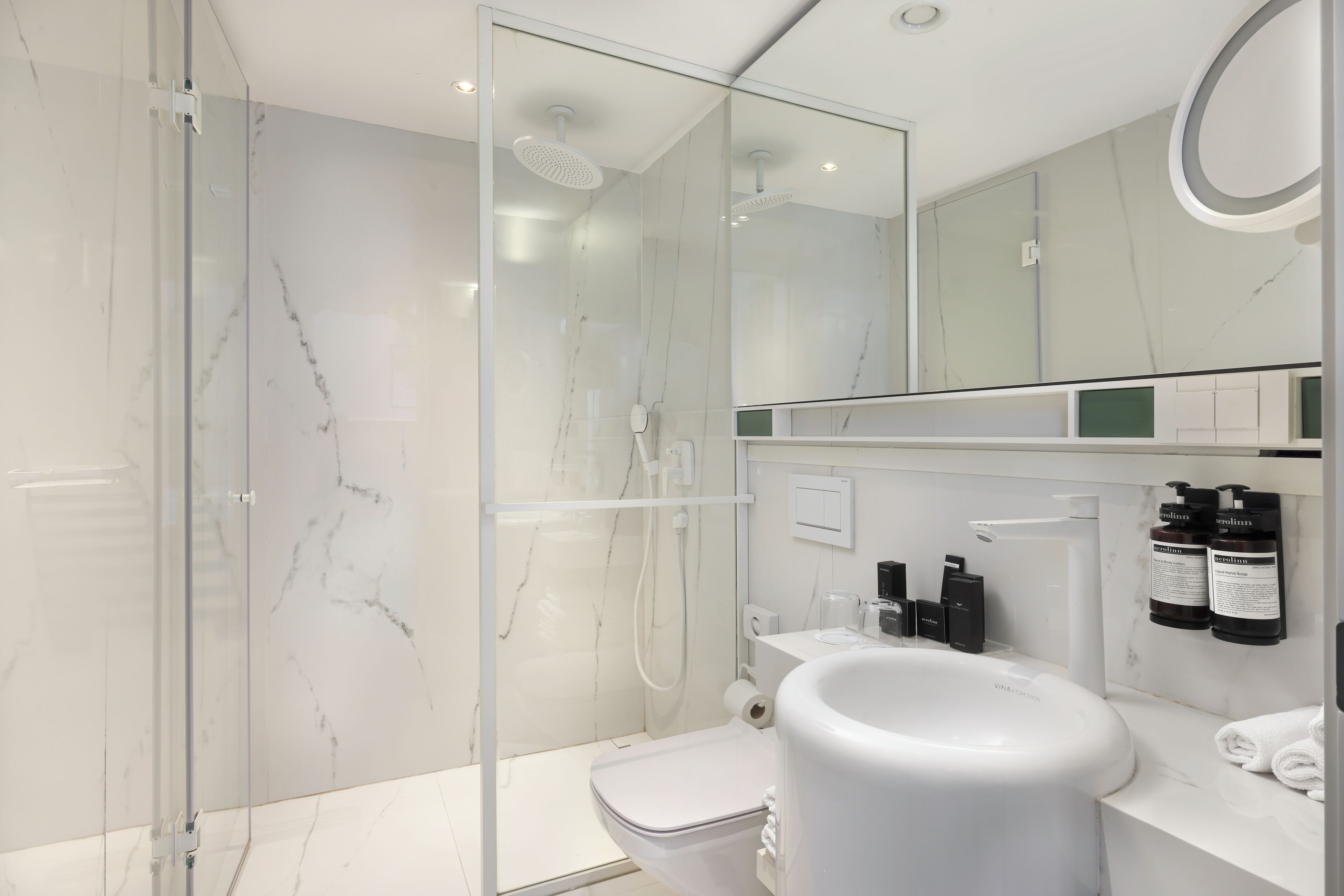 Ein modernes Badezimmer mit einer gläsernen Duschkabine, einer weißen Toilette und einem Waschbecken mit Pflegeprodukten.
