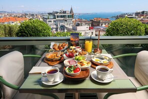 Una mesa de desayuno con una variedad de alimentos y bebidas, con vistas a un paisaje urbano que incluye edificios y una masa de agua.