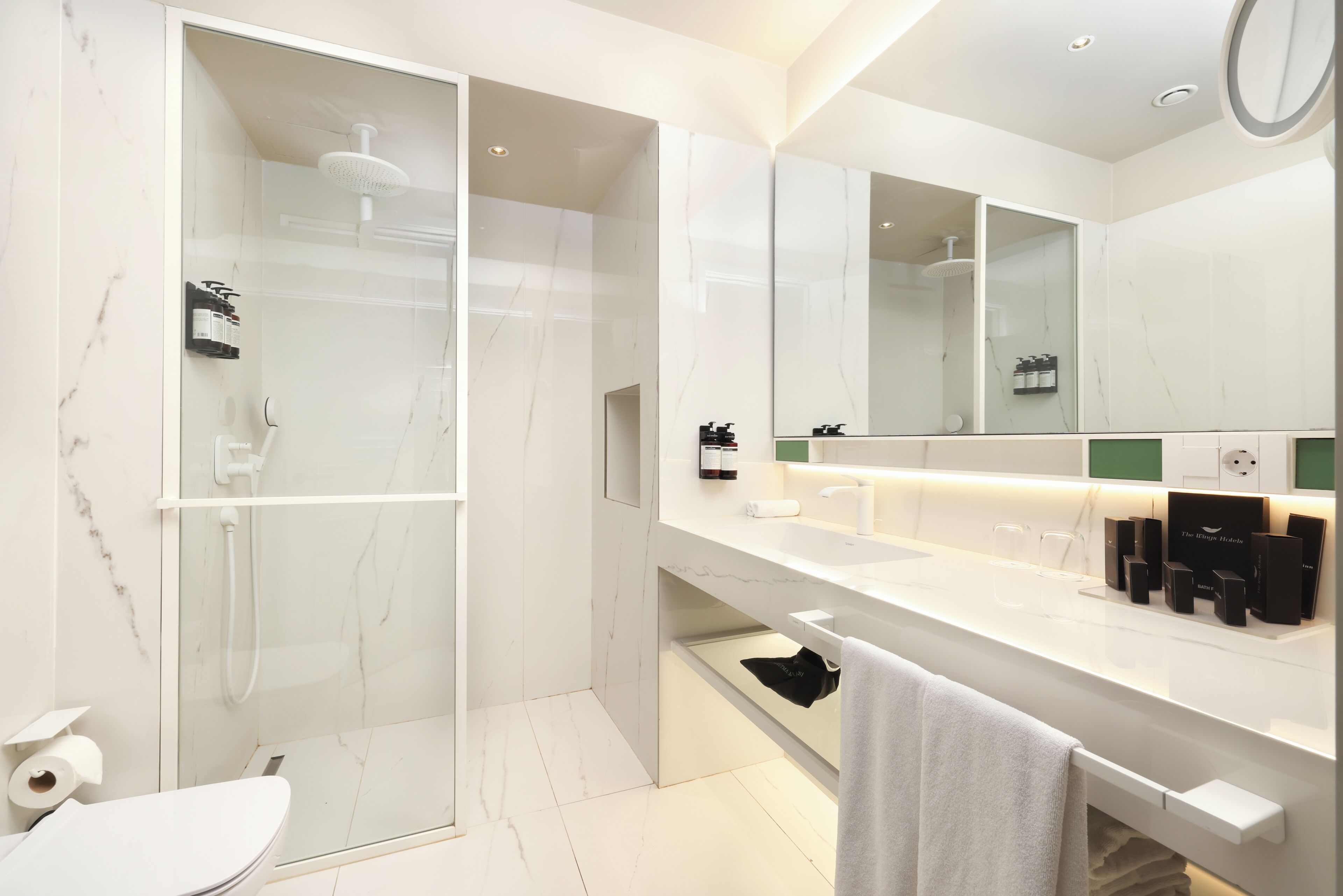 Un baño moderno con ducha envuelta en vidrio, un lavamanos blanco con espejo y artículos de aseo en la encimera.
