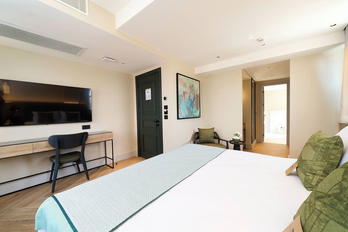 A hotel room with a bed, a desk, a chair, a television, and a painting on the wall.