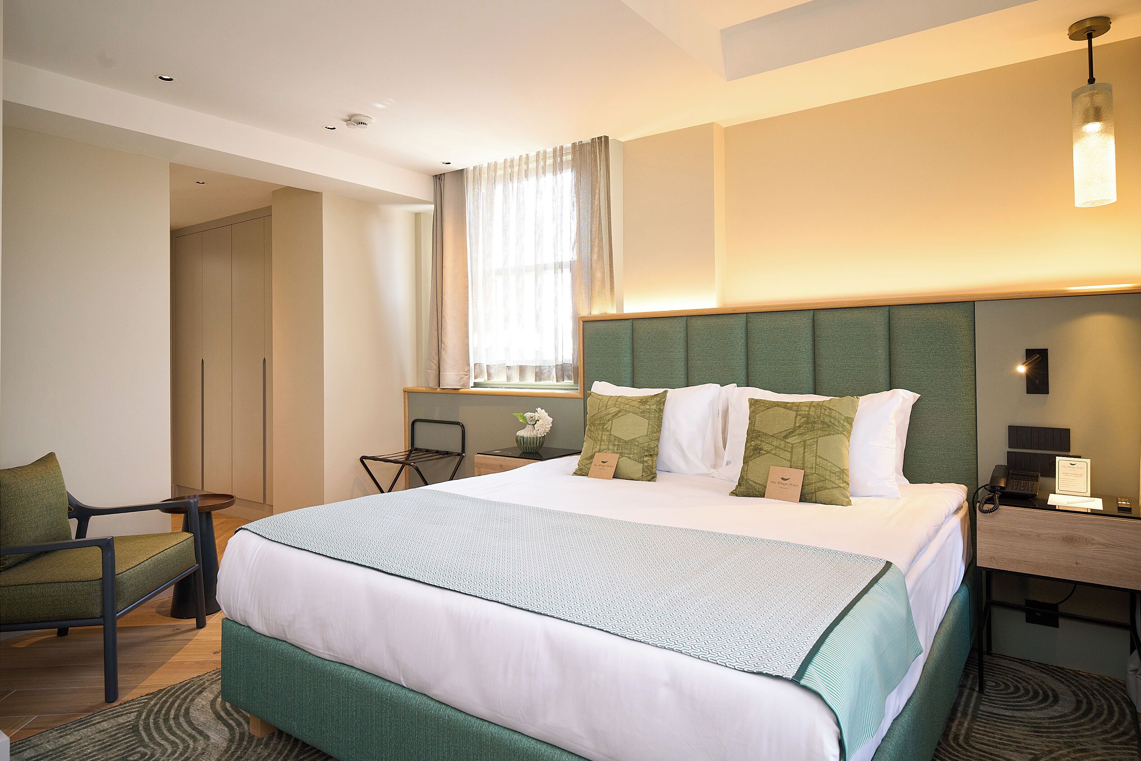 A hotel room with a large bed, a chair, a desk, and a window with curtains.