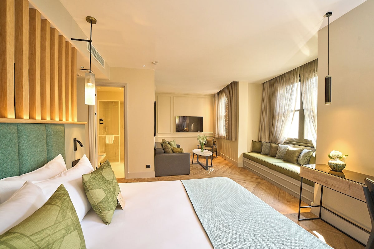 A modern hotel room with a large bed, a sofa, a small table, and a TV.