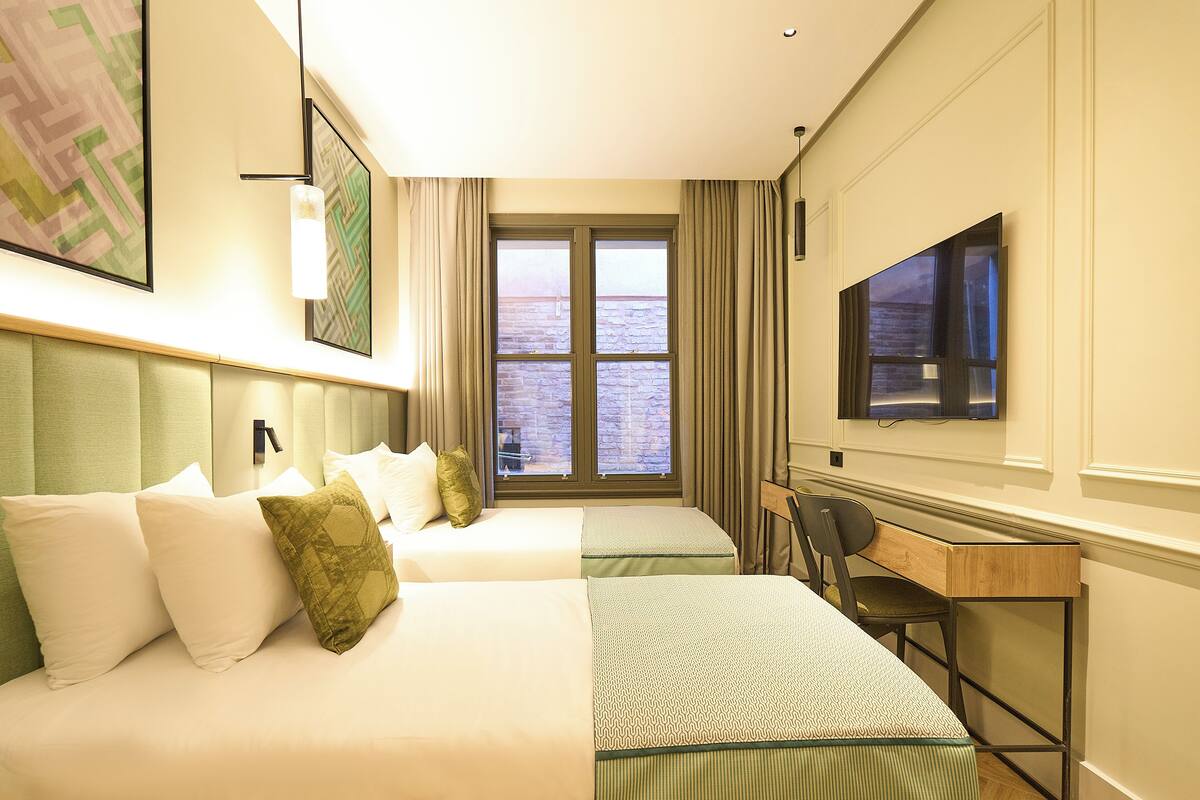 A hotel room with two beds, a desk, a chair, a TV, and a window with curtains.