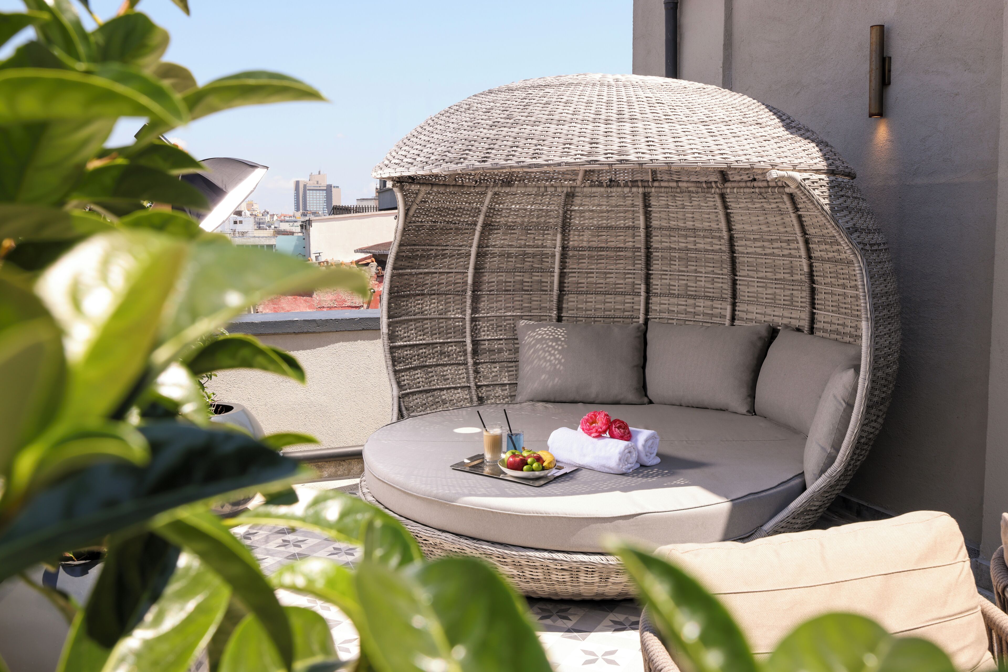 Un espacio de estar exterior de mimbre con cojines y una mesa con frutas y una bebida.