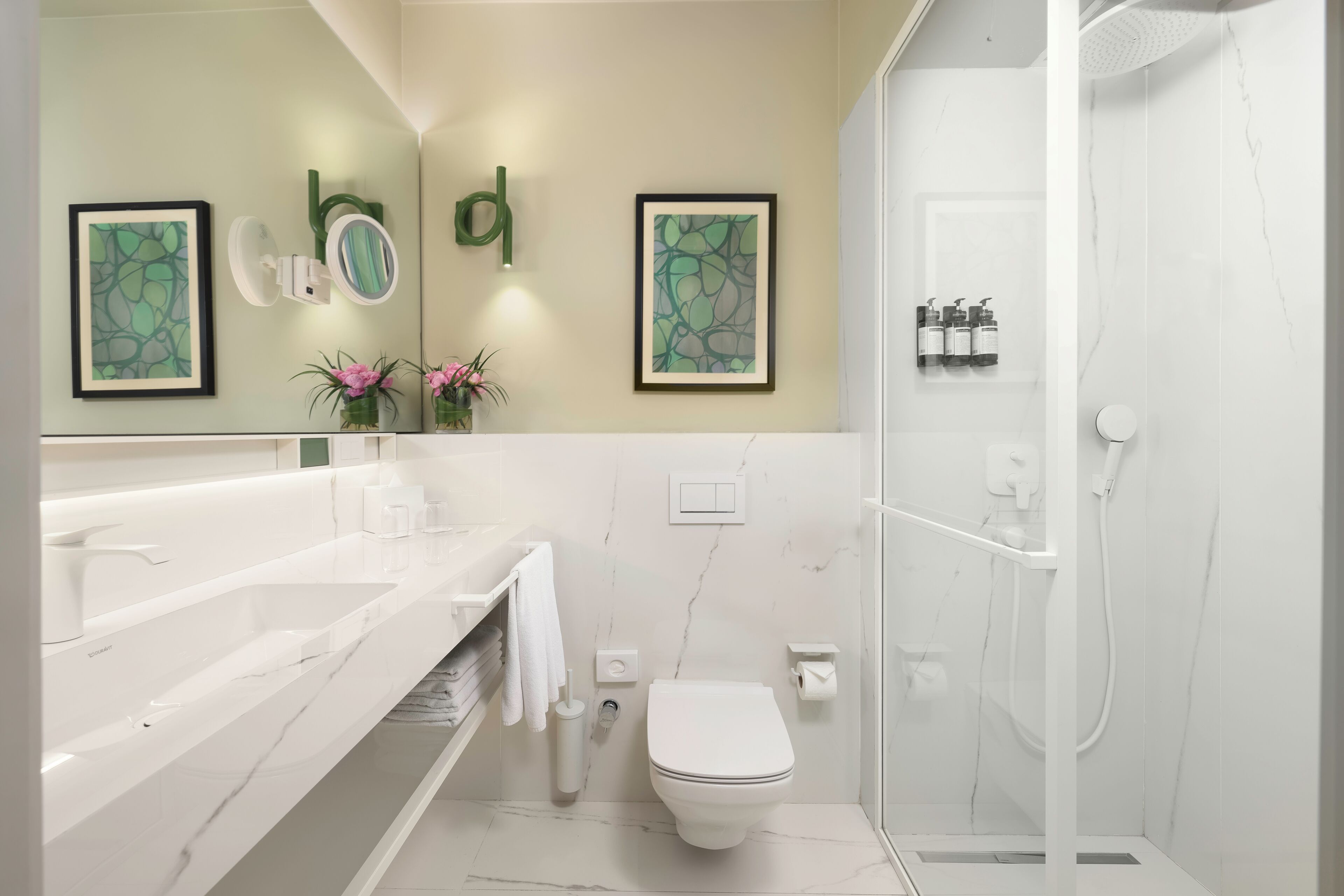 A modern bathroom with a white marble floor, a white toilet, a shower area, and two framed artworks on the wall.