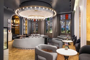 A modern lounge area with a circular light fixture, seating arrangements, and a view through large windows. - The Wings Hotels Pera (İstanbul)