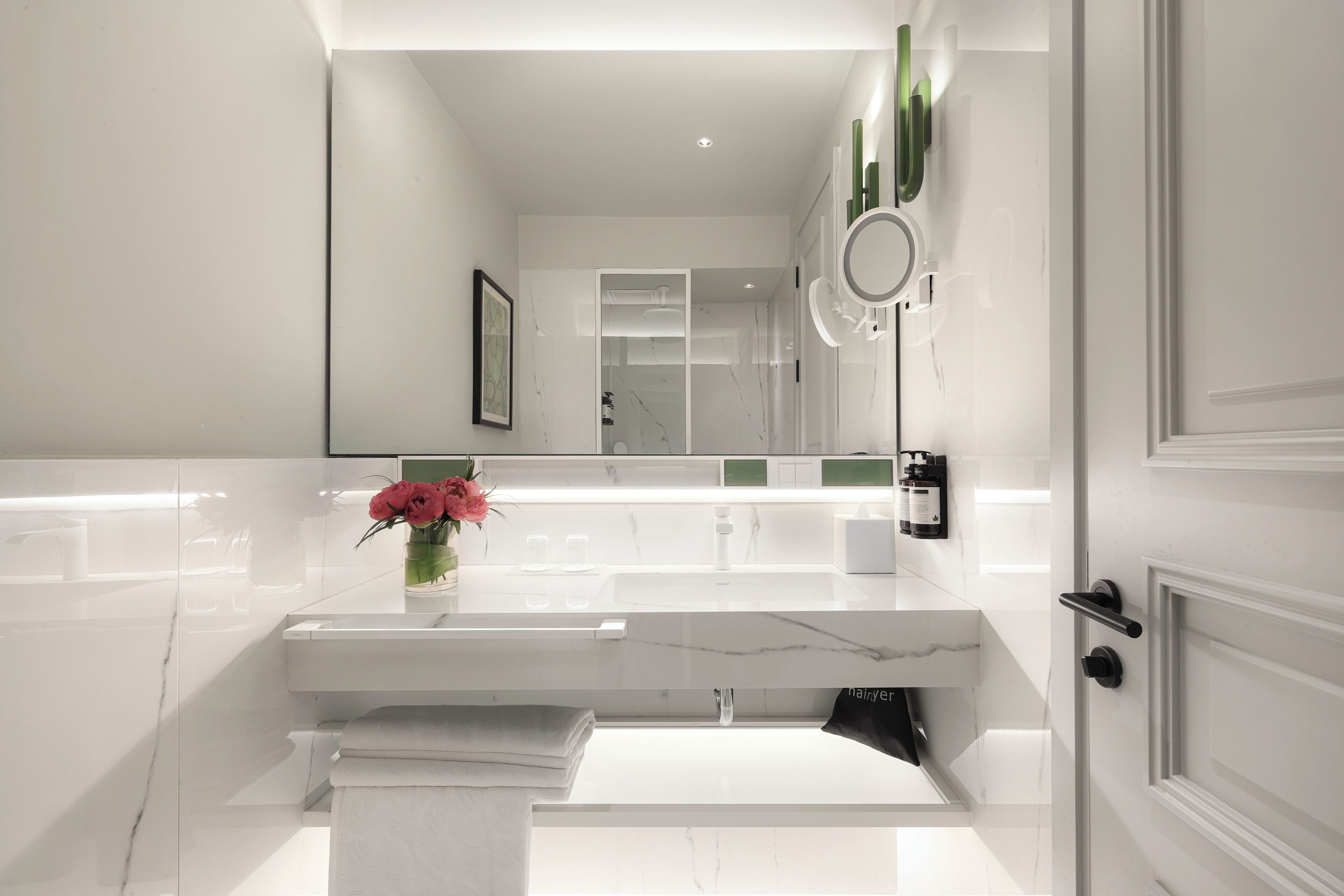 Une salle de bain moderne avec un meuble-lavabo en marbre, un grand miroir et une œuvre d’art encadrée accrochée au mur.