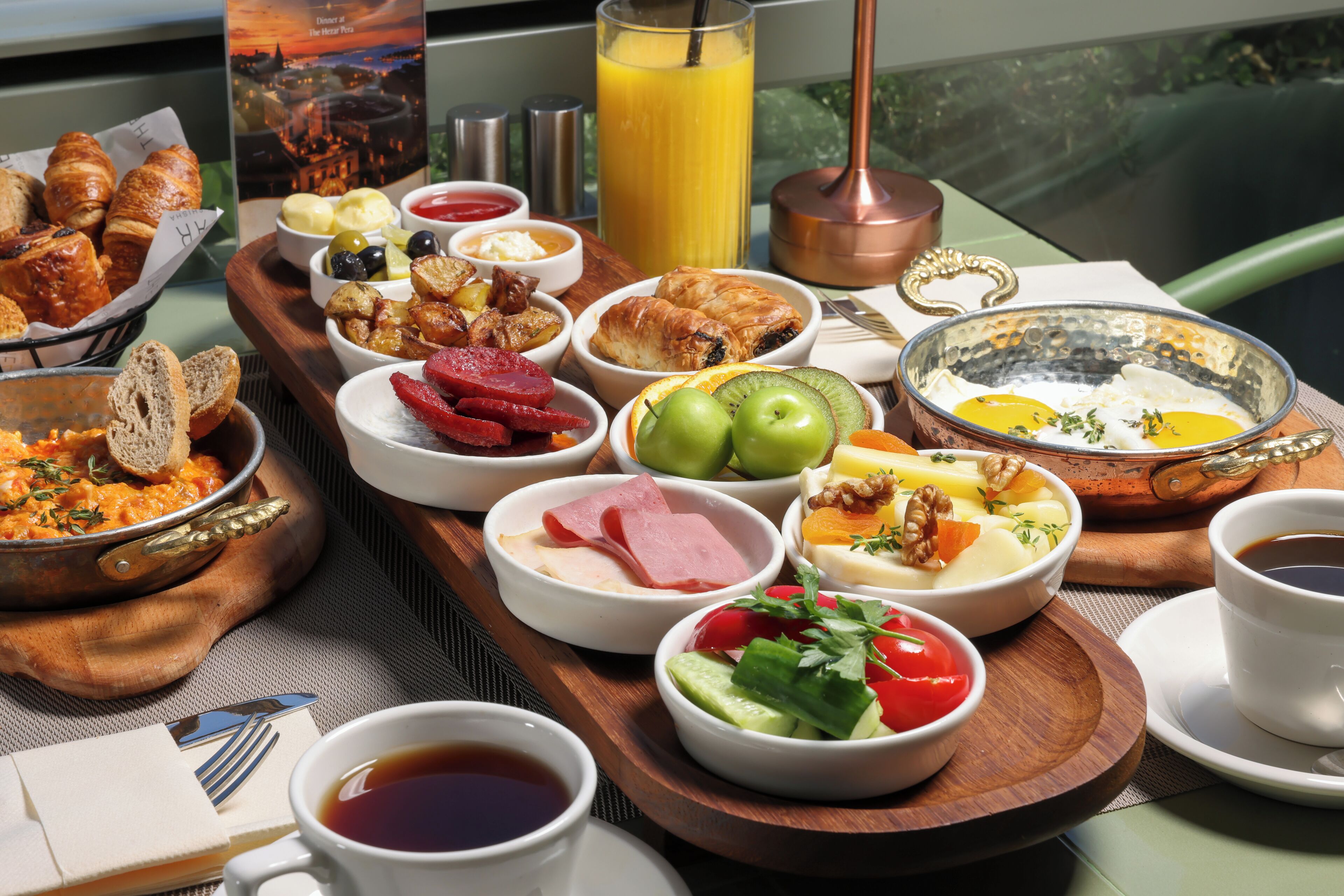 A breakfast tray with croissants, ham, eggs, and fruit.