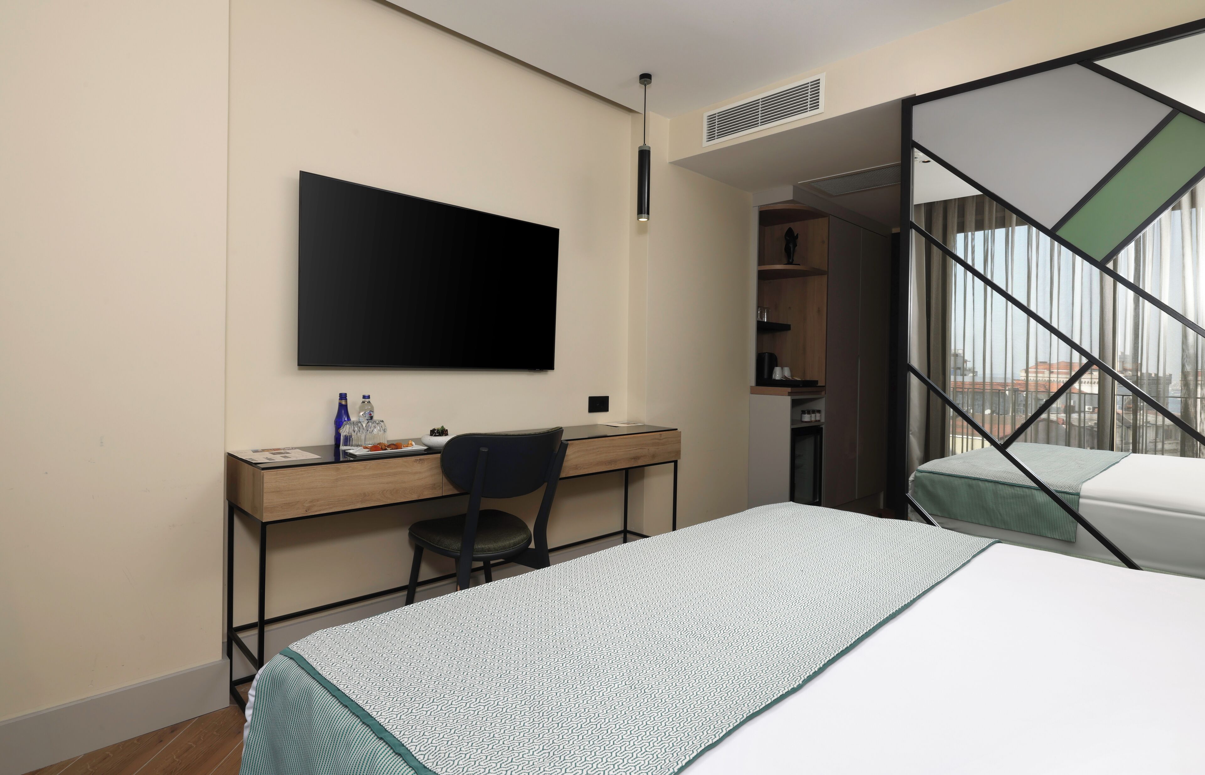 A hotel room with a bed, a desk with a chair, a flat-screen TV, and a window with a view.