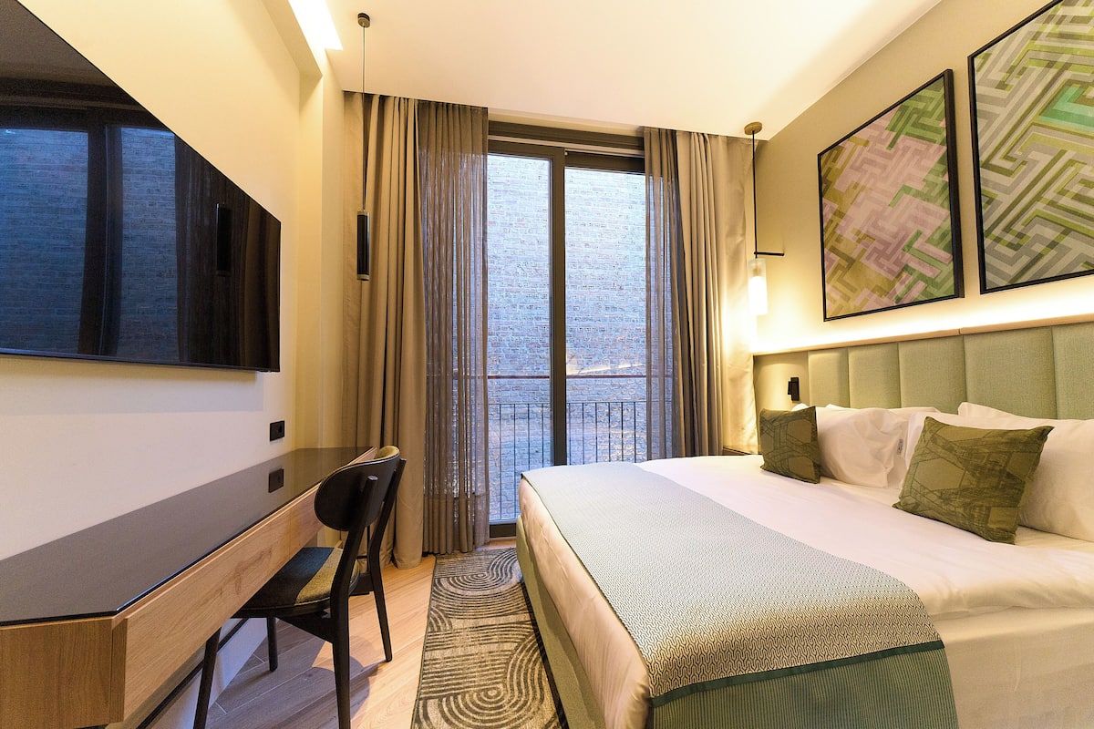 A hotel room with a bed, desk, chair, and a large window.