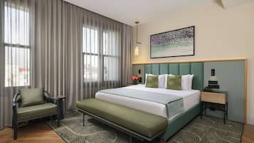 A hotel room with a bed, a chair, a nightstand, a lamp, and a painting on the wall.