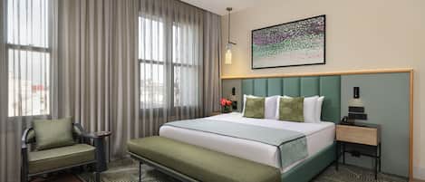 Habitación de hotel con cama, una silla, mesita de noche, lámpara y un cuadro en la pared.