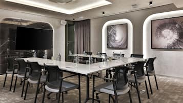 A conference room with a long table, chairs, a flat-screen TV, and two abstract paintings on the walls.