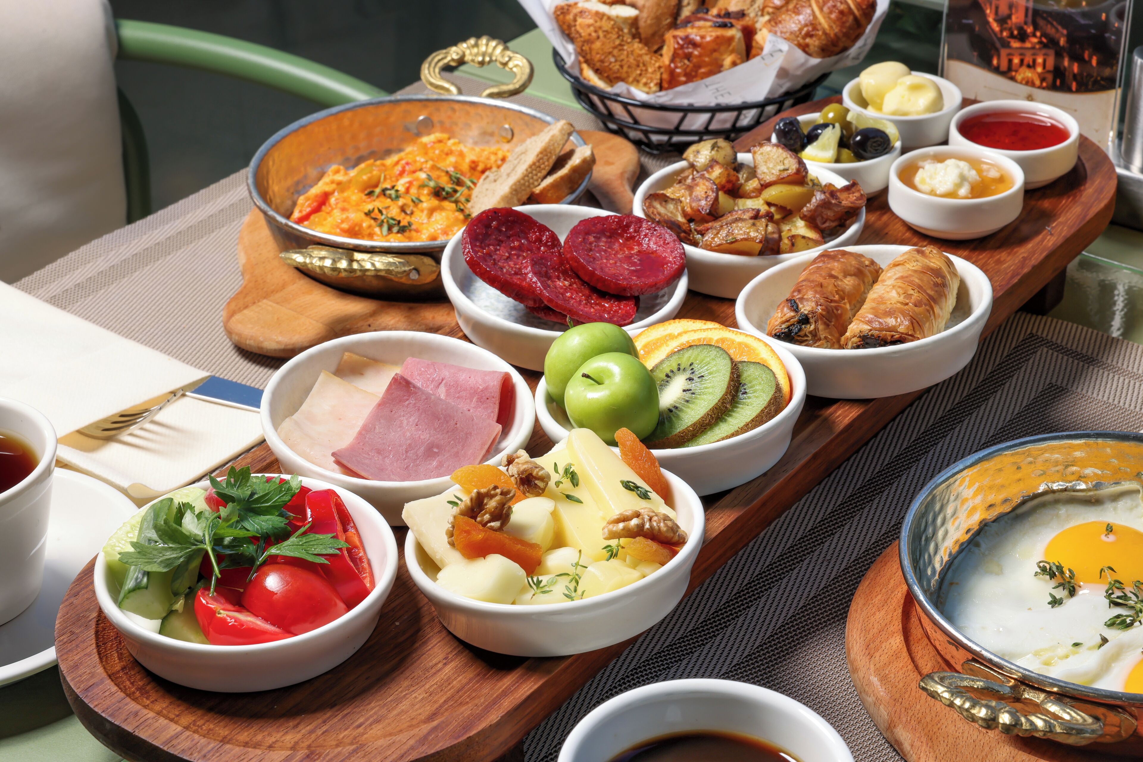 A breakfast buffet with various dishes including meats, cheeses, fruits, and pastries.