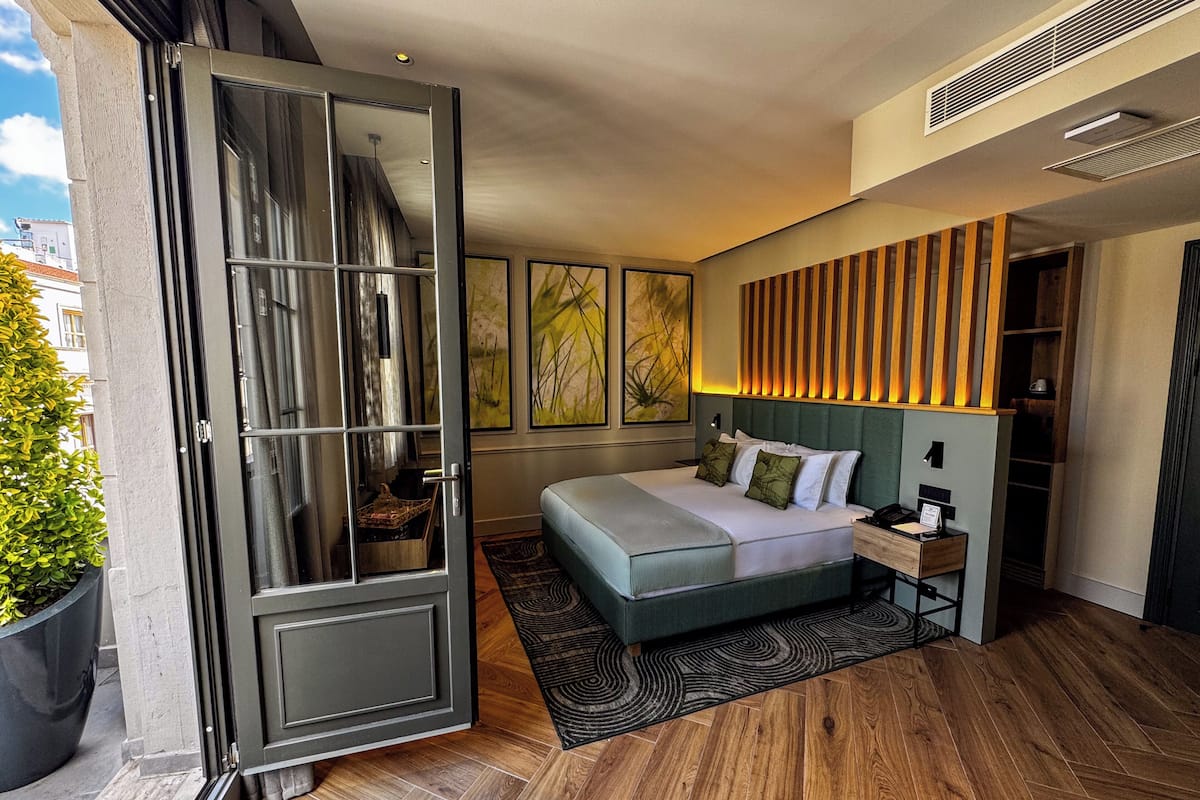 A modern hotel room with a large bed, a wooden headboard, and a sliding glass door leading to an outdoor area.