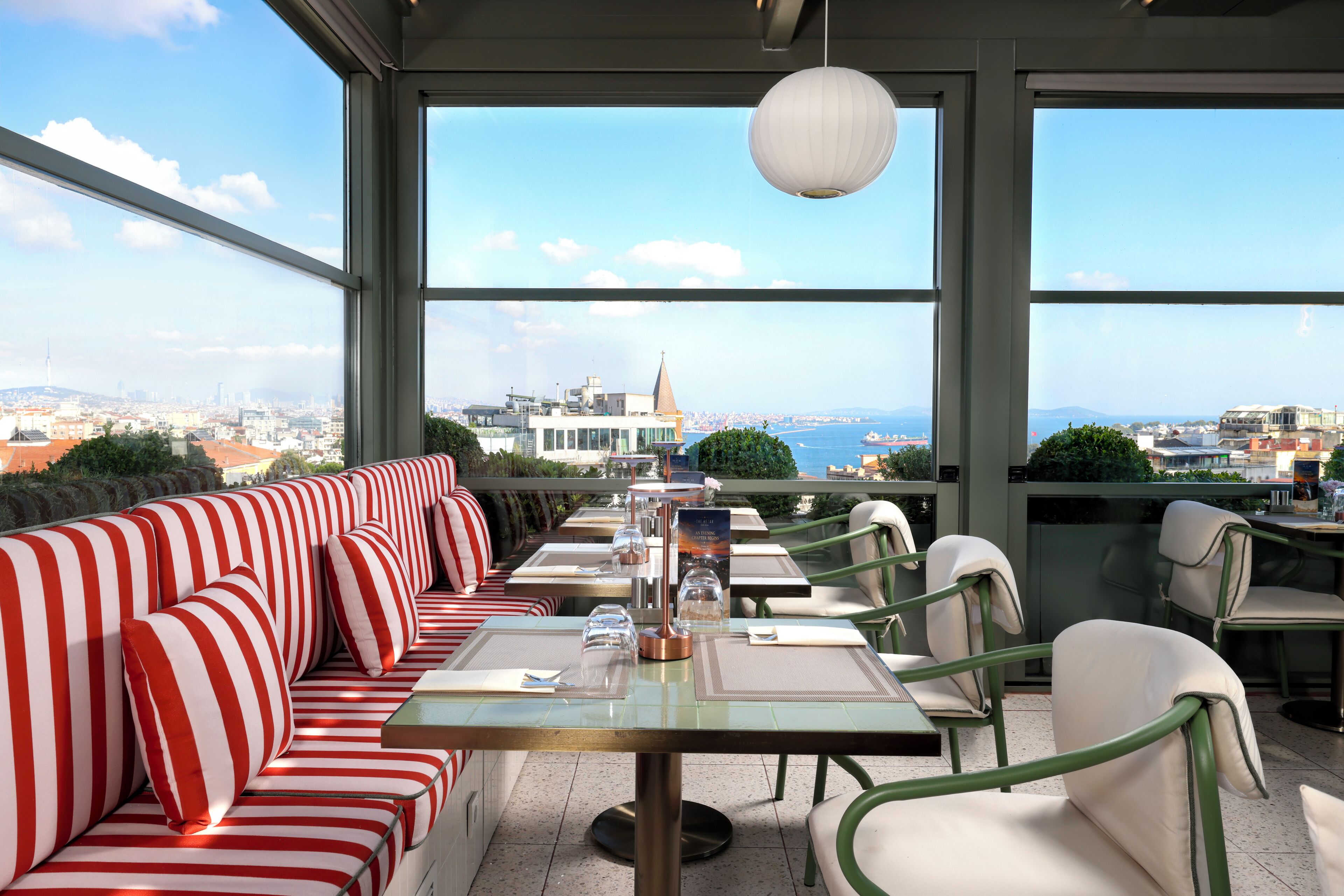 A rooftop dining area with a view of a cityscape, featuring striped seating and tables.