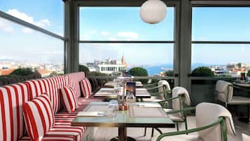 A rooftop dining area with a view of a cityscape, featuring striped seating and tables.