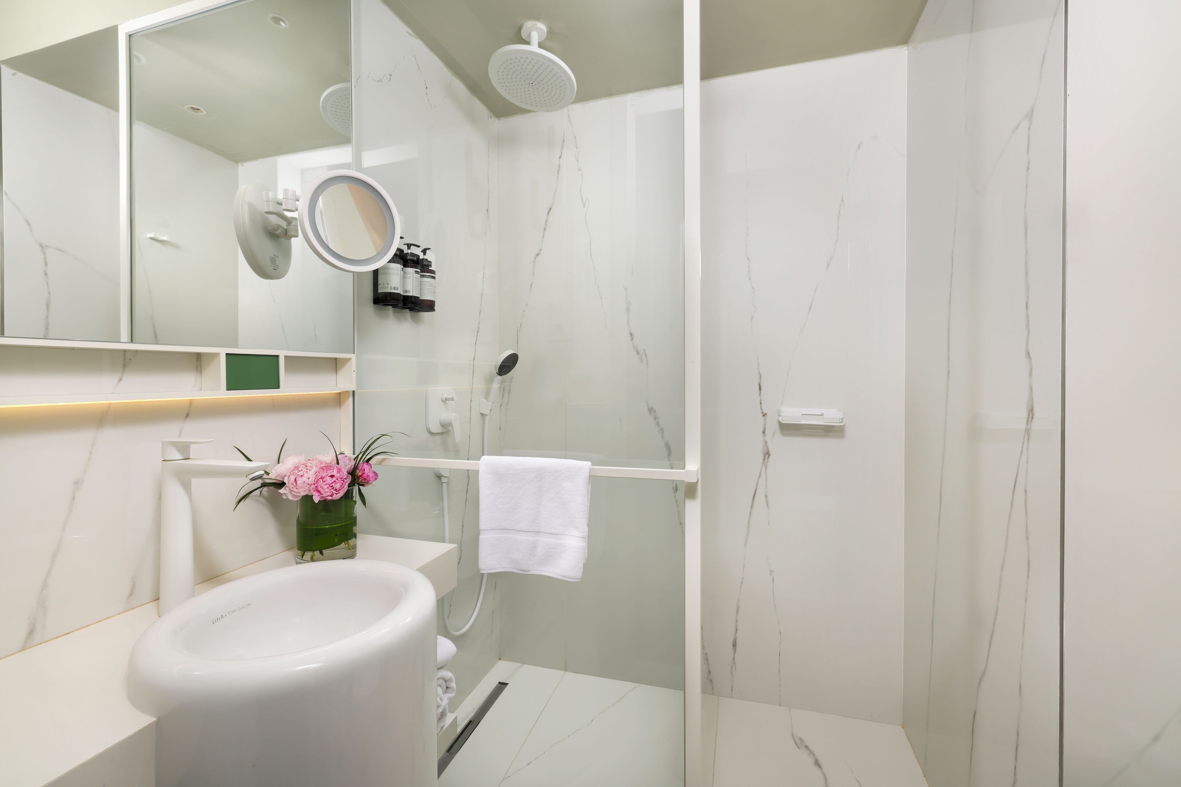 Un baño moderno con un lavamanos blanco, un espejo, una ducha y un perchero para toallas.