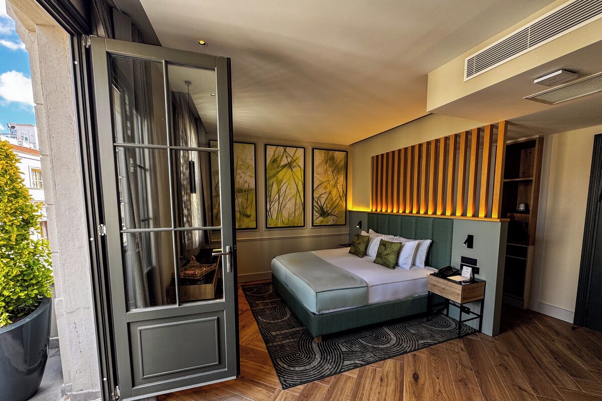 A modern hotel room with a large bed, a wooden headboard, and a sliding glass door leading to an outdoor area.