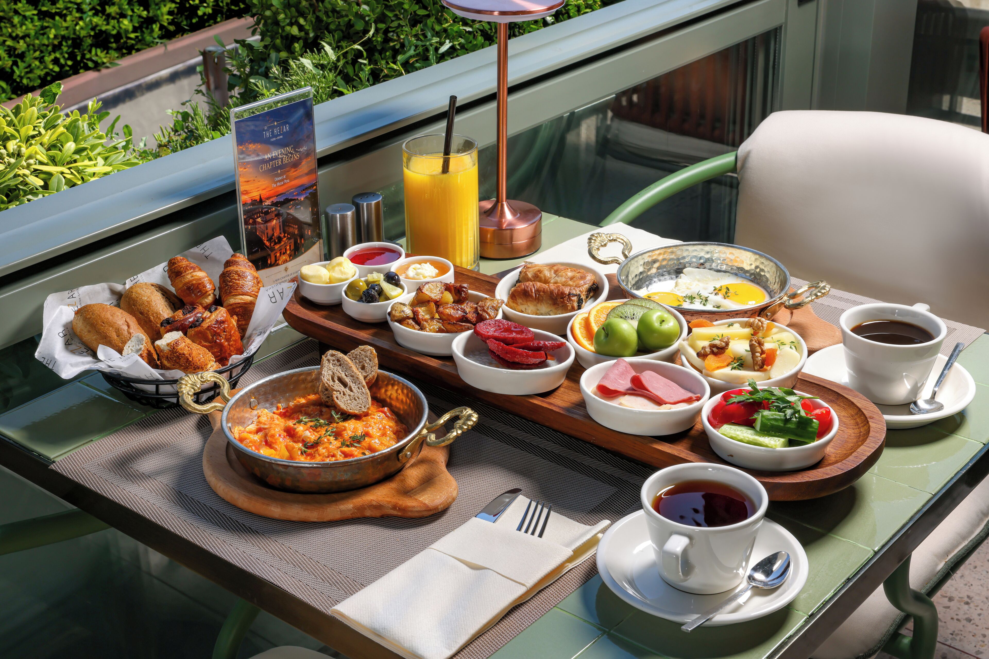 A breakfast buffet with various dishes, a menu sign, and a glass of orange juice on a table.