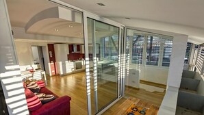 A modern living room with a red sofa, a wooden coffee table, and a glass sliding door leading to a balcony with a city view.