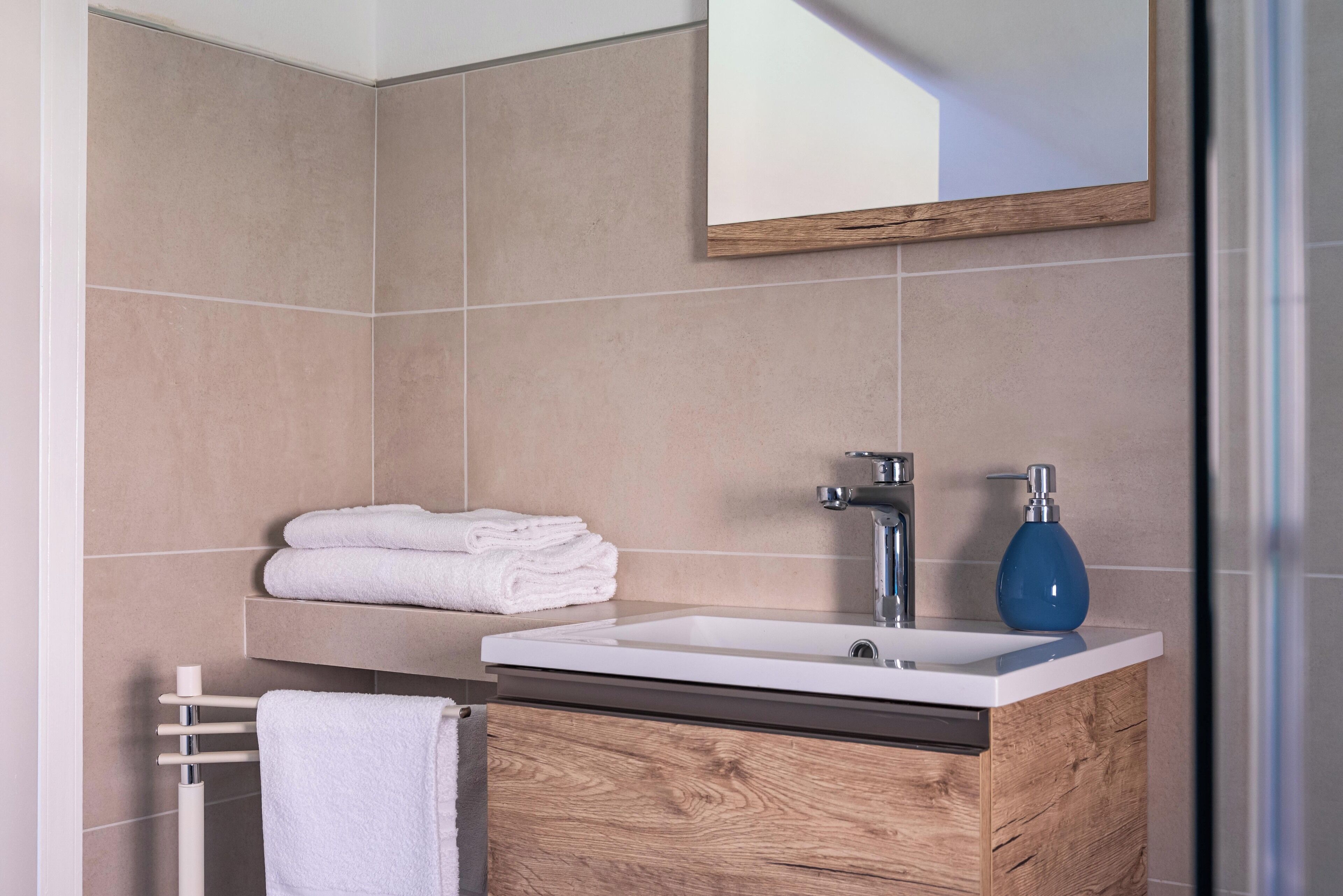 A modern bathroom with a wooden vanity, a white sink, and a blue soap dispenser.