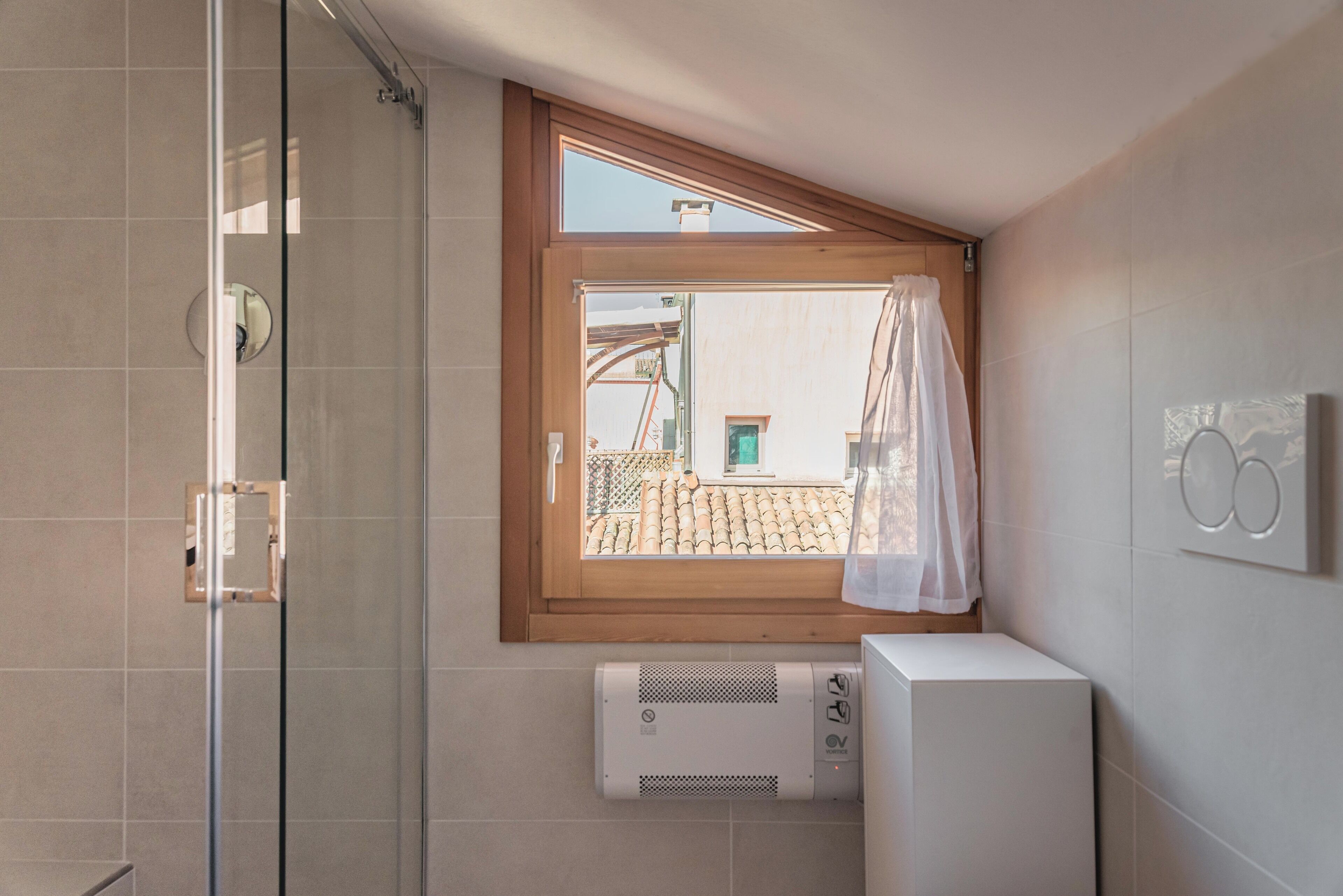 Ein Badezimmer mit Dusche, einem Fenster mit Vorhang und einer Wandklimaanlage.