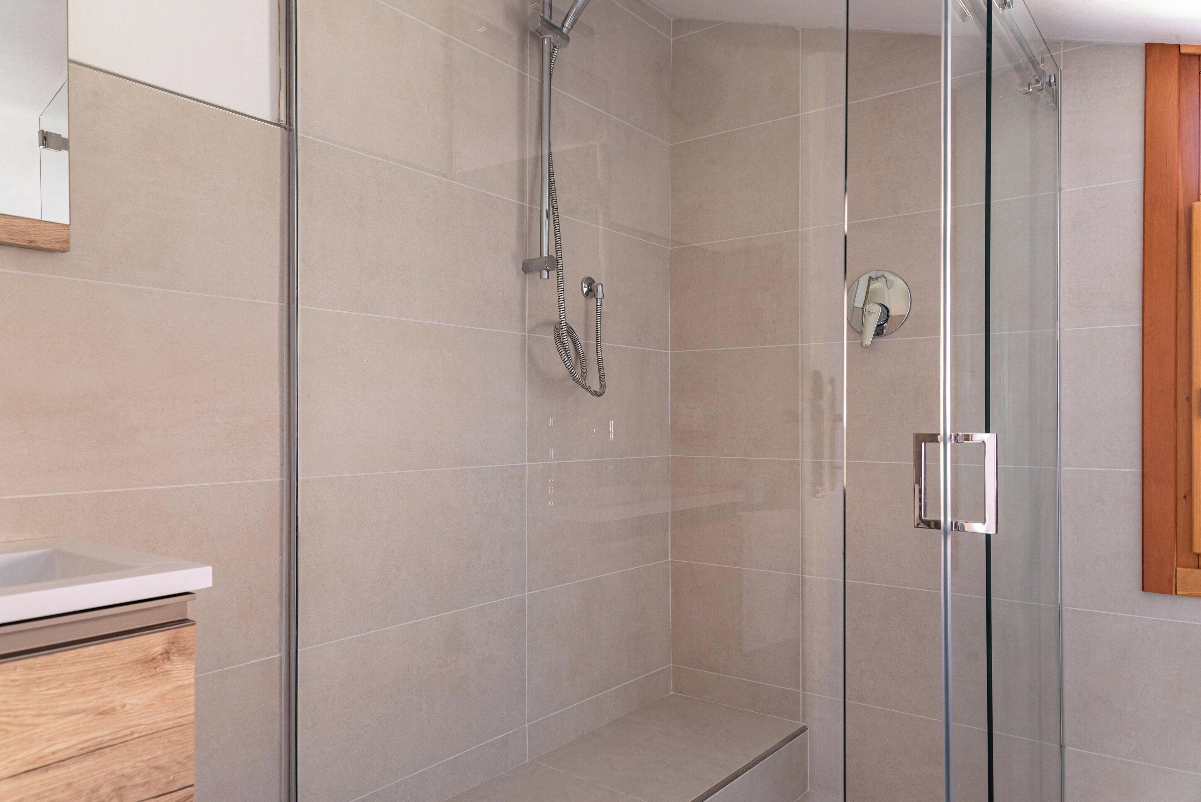 A modern bathroom with a glass shower enclosure, a wooden cabinet, and a mirror.