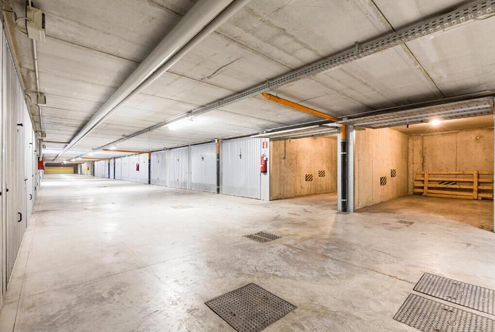 A long, empty parking garage with concrete floors and walls, metal beams, and fire extinguishers.
