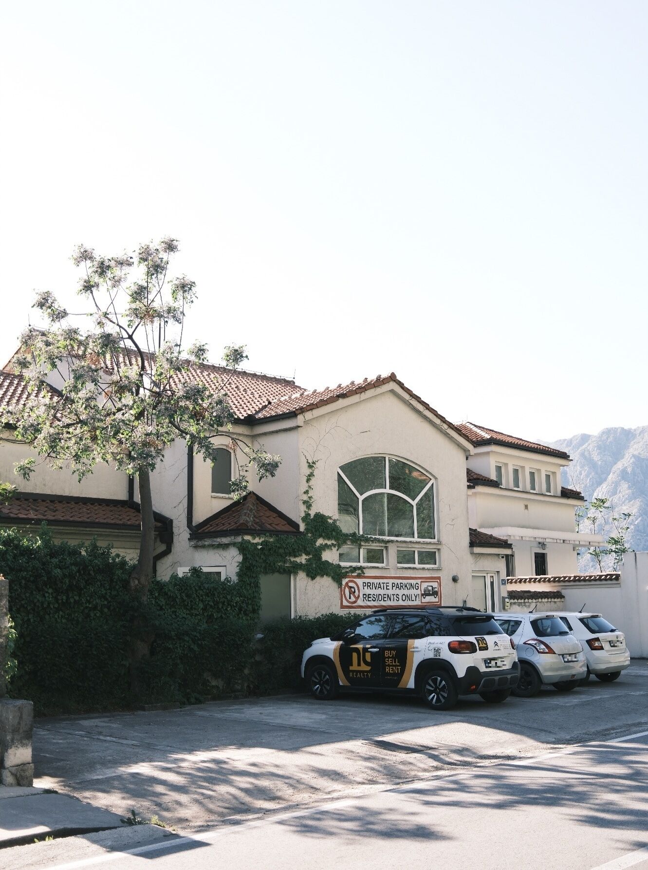 A building with a sign indicating private parking for residents only, parked cars, and a mountainous backdrop.