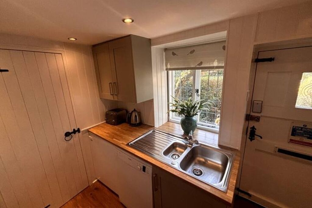 A compact kitchen with a double sink, wooden countertop, and a window with a view of greenery.