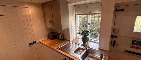 A compact kitchen with a double sink, wooden countertop, and a window with a view of greenery.