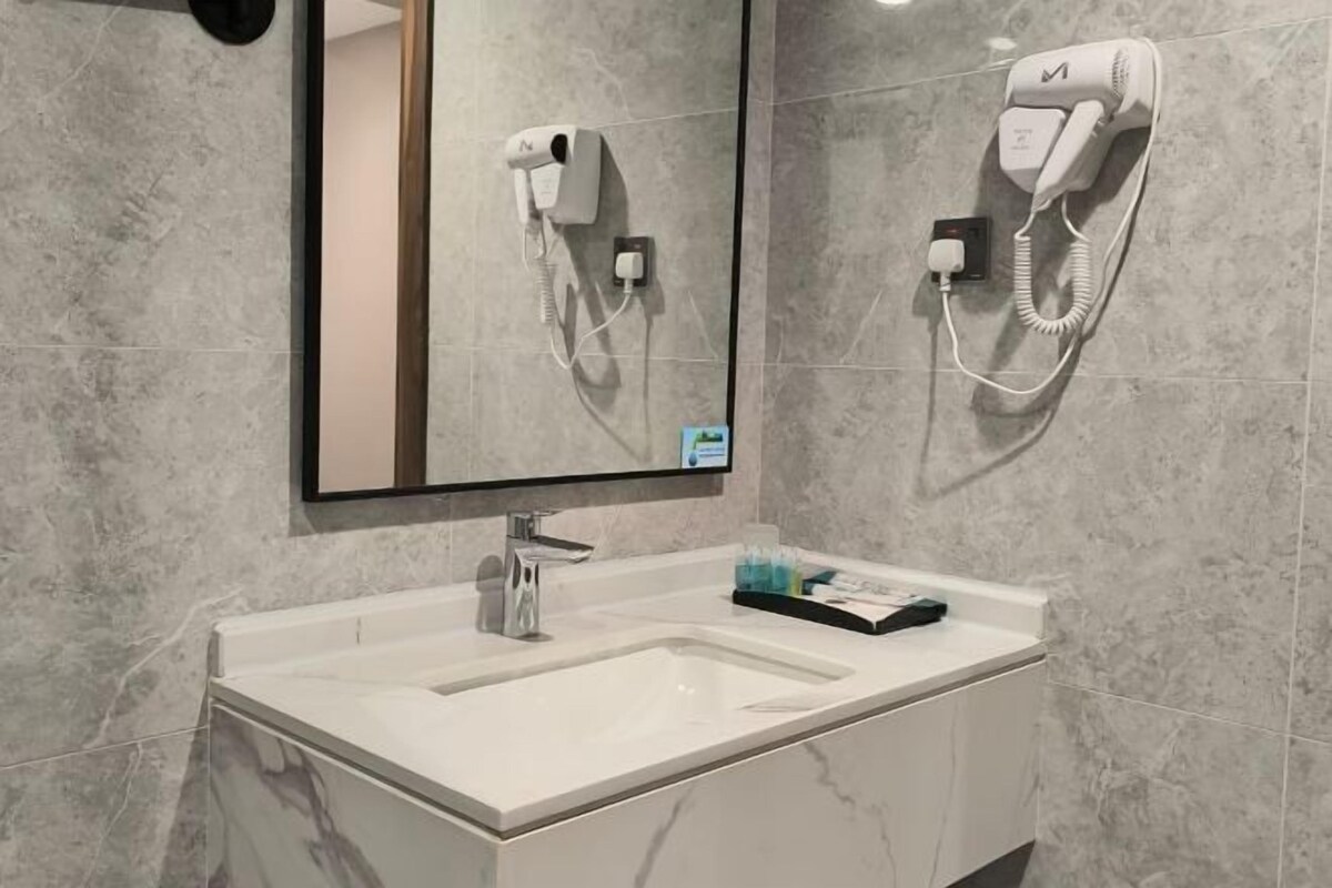 Un baño moderno con un lavamanos blanco, un espejo y dos secadores de pelo fijados a la pared.