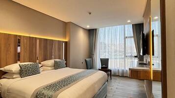 A modern hotel room with a large bed, a desk, a chair, and a TV.
