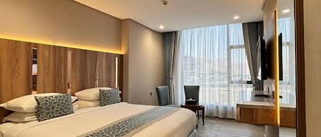 A modern hotel room with a large bed, a desk, a chair, and a TV.