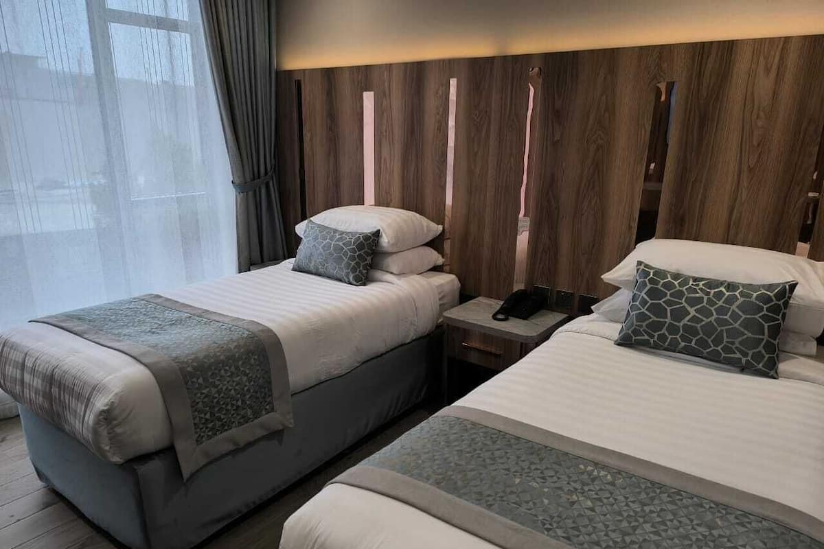Habitación de hotel con dos camas, una mesita de noche y un cabecero de madera.