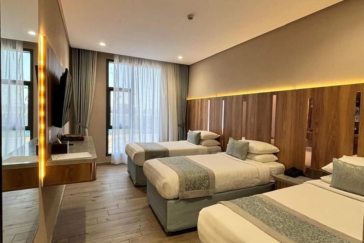 Una habitación de hotel con tres camas, suelo de madera, un espejo grande y un televisor.