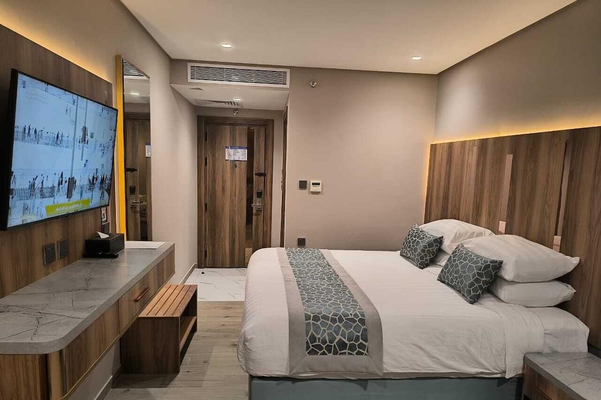 Una habitación de hotel moderna con una cama grande, un televisor montado en la pared y un banco de madera.
