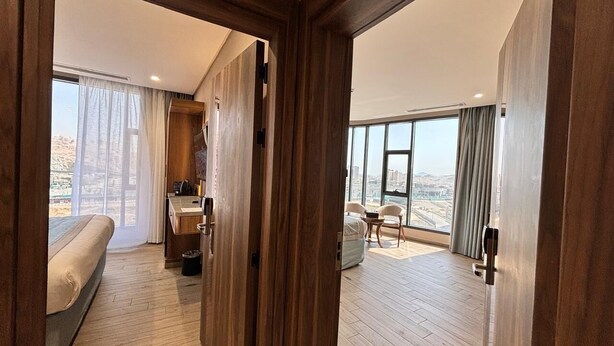 Une chambre d’hôtel comprenant un lit, un bureau avec une chaise, une petite table et une vue sur la ville grâce à de grandes fenêtres.