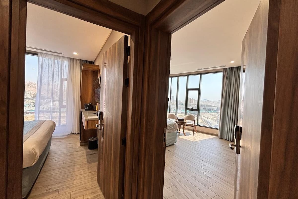 Habitación de hotel con cama, escritorio con silla, una mesita y vistas a la ciudad a través de amplias ventanas.
